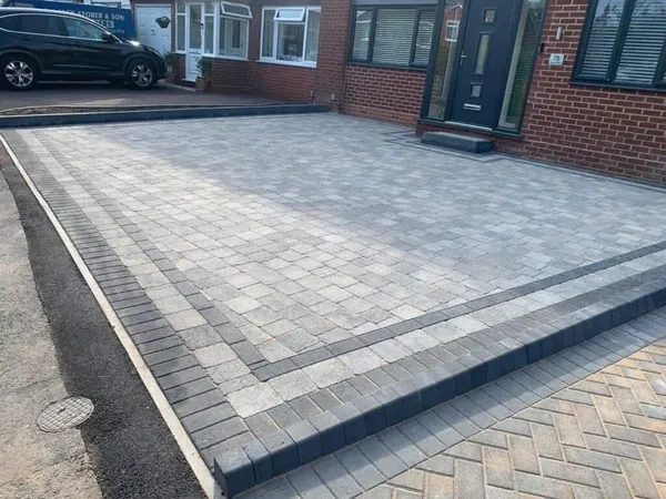 Silver-grey block paving driveway with a charcoal border in front of a red-brick house