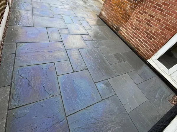 Wet slate-grey riven patio slabs laid along the side of a brick house